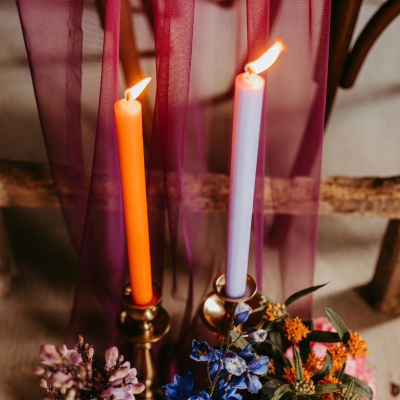 two taper candles of different colors with vibrant flowers