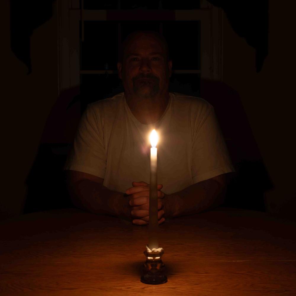 Man sits at a table with a single candle to show how dark it is