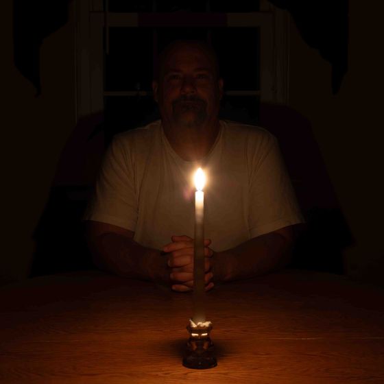 Man sits at a table with a single candle to show how dark it is