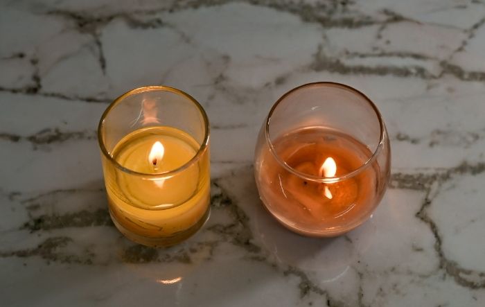Two lit votive candles, one in a narrow cup and one in a wider cup