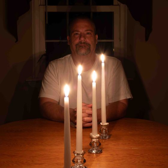 man sits at a table with 4 candles to show the light they give off in comparison to 1