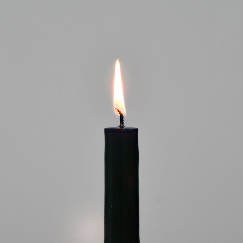 Lit taper candle against a grey background