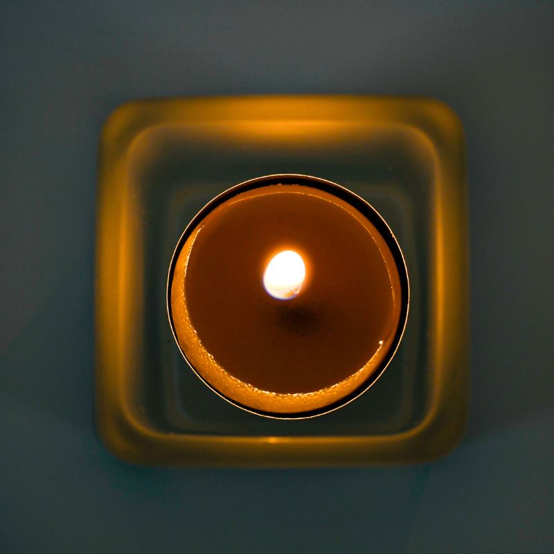Lit tealight candle in a square cup