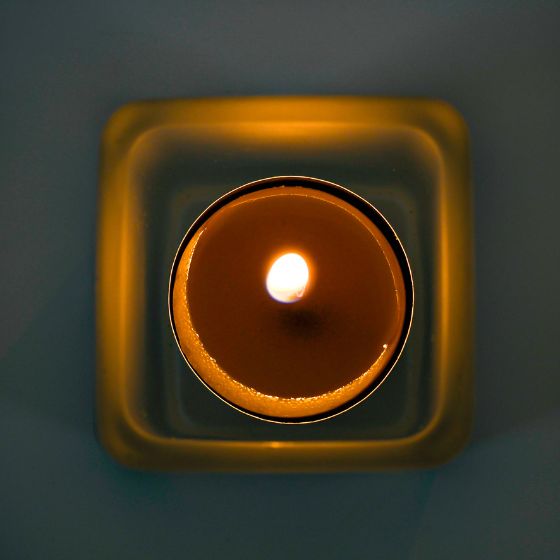 Lit tealight candle in a square cup